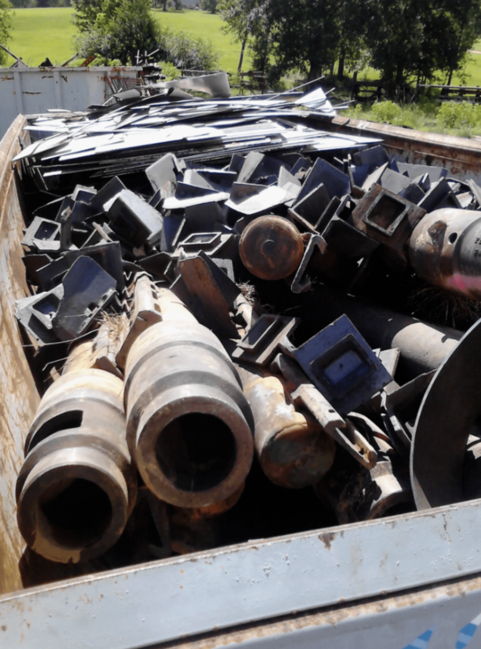 Heavy carbon-steel pipe and cast iron loaded into an open-top roll-off container by the CW Mobile Service crew, ready to roll out